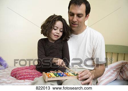 A young girl sitting with her father and playing the xylophone View Large Photo Image Stock Image - A young girl sitting with her father and playing the xylophone. Fotosearch