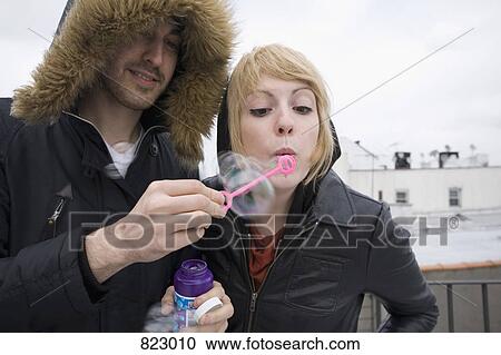 Stock Image - A young couple blowing bubbles on a rooftop. Fotosearch
