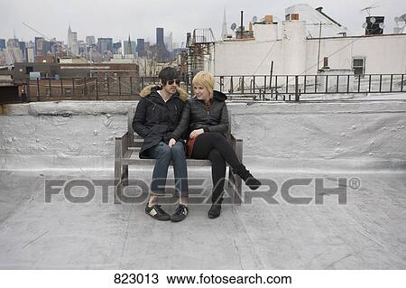 A young couple sitting on a bench on a rooftop View Large Photo Image Stock Image - A young couple sitting on a bench on a rooftop. Fotosearch