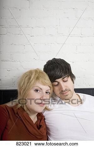A young couple sitting on a sofa holding drinks View Large Photo Image Stock Image - A young couple sitting on a sofa holding drinks. Fotosearch