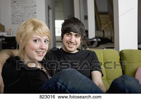 A young couple sitting on a sofa View Large Photo Image Stock Photograph - A young couple sitting on a sofa. Fotosearch