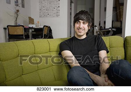 A young man sitting on a sofa View Large Photo Image Stock Image - A young man sitting on a sofa. Fotosearch