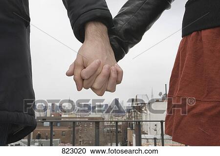Stock Image - Detail of a young couple standing on a roof top holding hands. Fotosearch