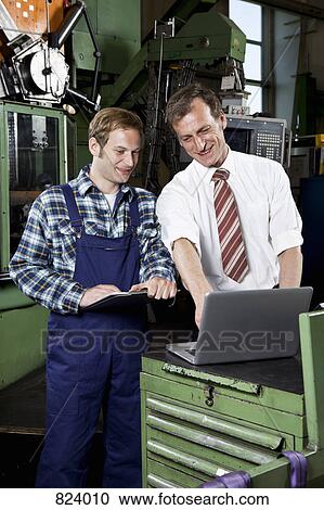 Stock Image - A factory manager and a factory worker looking at a laptop and laughing. Fotosearch
