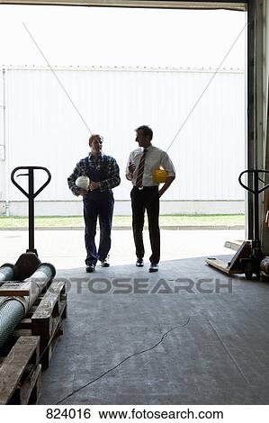 Stock Photograph - A manager talking to a manual worker in a warehouse doorway, back lit. Fotosearch