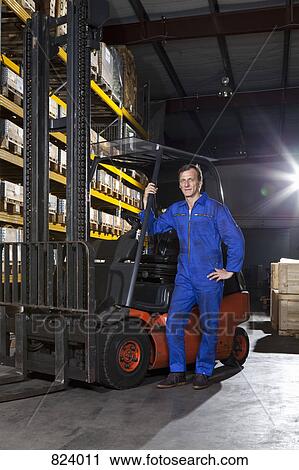 A manual worker standing next to a forklift in a metal parts warehouse View Large Photo Image Stock Image - A manual worker standing next to a forklift in a metal parts warehouse. Fotosearch