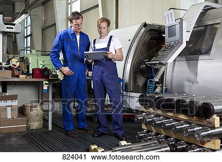 Stock Image - Two manual workers in a metal parts factory. Fotosearch