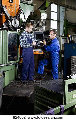 Two men in a metal parts factory reviewing a clipboard View Large Photo Image Stock Image - Two men in a metal parts factory reviewing a clipboard. Fotosearch