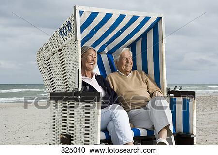 Stock Image - A senior couple sitting together in a hooded beach chair. Fotosearch
