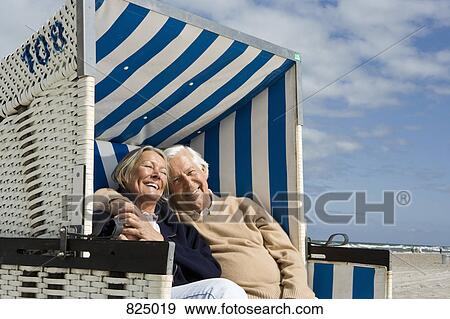 A senior couple sitting together in a hooded beach chair View Large Photo Image Stock Photo - A senior couple sitting together in a hooded beach chair. Fotosearch