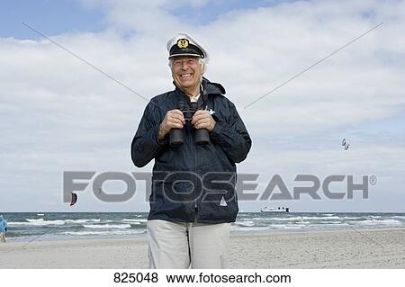 A senior man on a beach holding binoculars View Large Photo Image Stock Photo - A senior man on a beach holding binoculars. Fotosearch