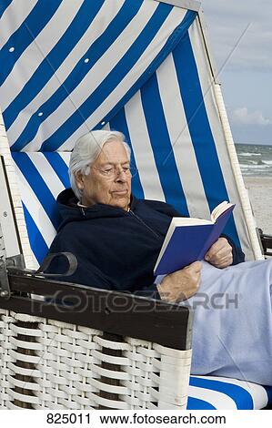 Stock Image - A senior man sitting in a hooded beach chair, reading. Fotosearch