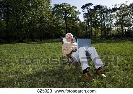 A senior man sitting in a lounge chair using a laptop, outdoors View Large Photo Image Stock Image - A senior man sitting in a lounge chair using a laptop, outdoors. Fotosearch