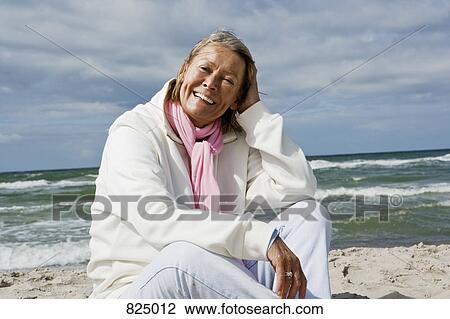 A senior woman sitting on a beach View Large Photo Image Stock Image - A senior woman sitting on a beach. Fotosearch