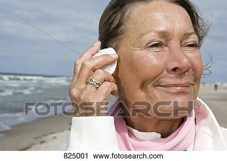A senior woman with a seashell to her ear View Large Photo Image Stock Image - A senior woman with a seashell to her ear. Fotosearch