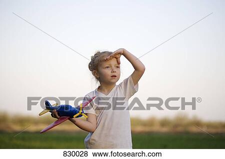 A portrait of a young girl holding a toy airplane and shielding her eyes, outdoors View Large Photo Image Stock Photo - A portrait of a young girl holding a toy airplane and shielding her eyes, outdoors. Fotosearch