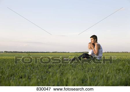 Stock Photo - Side view of a woman and a girl sitting together in a field. Fotosearch