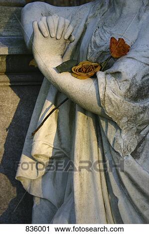 Stock Image - Detail of a statue adorned with roses. Fotosearch