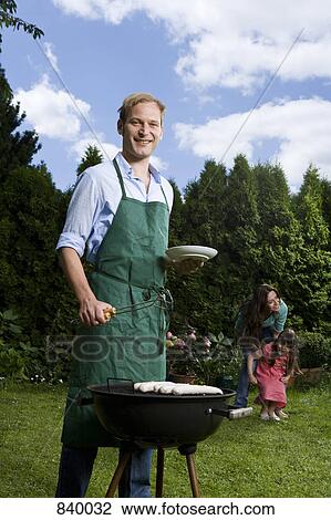 A man barbecuing bratwurst in a back yard, wife and child in the background View Large Photo Image Stock Image - A man barbecuing bratwurst in a back yard, wife and child in the background. Fotosearch