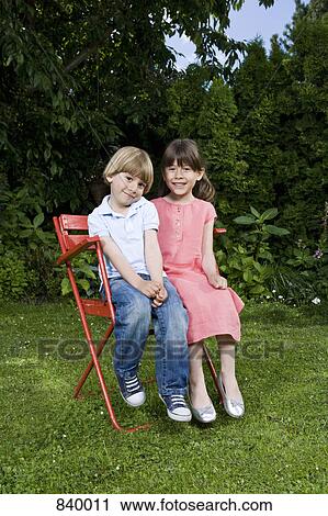 Stock Image - A young brother and sister sitting on a chair, outdoors. Fotosearch