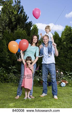 Stock Photo - Two parents and their two children holding balloons, outdoors. Fotosearch