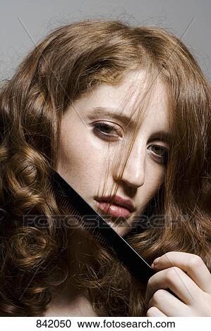 Stock Image - Portrait of a young woman combing her hair. Fotosearch