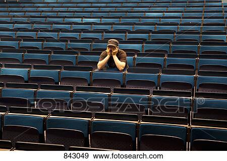 Stock Photo - A man sitting in an auditorium, hands covering eyes. Fotosearch