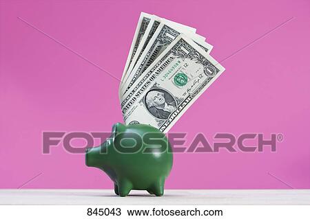 Stock Image - A green piggy bank with dollar bills sticking out of it. Fotosearch