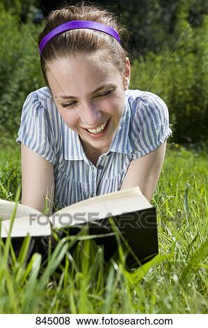 Stock Photo - A woman lying in grass reading a book. Fotosearch