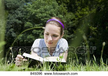 A woman lying in grass reading a book View Large Photo Image Stock Photograph - A woman lying in grass reading a book. Fotosearch