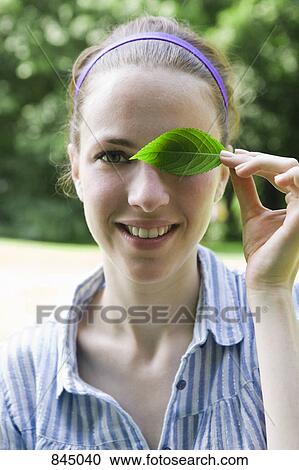 A young woman covering her eye with a leaf View Large Photo Image Stock Image - A young woman covering her eye with a leaf. Fotosearch