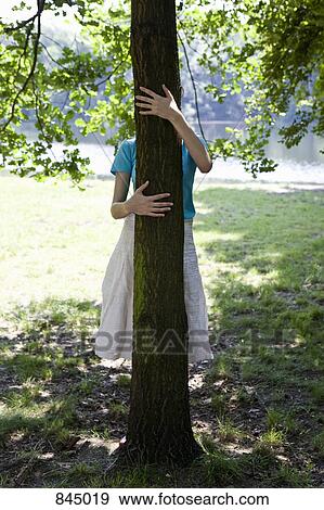Stock Photo - A young woman hugging a tree, obscured face. Fotosearch
