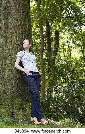A young woman leaning against a tree View Large Photo Image Picture - A young woman leaning against a tree. Fotosearch
