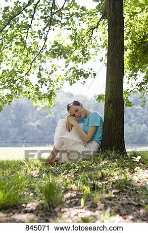 A young woman leaning against a tree next to a lake View Large Photo Image Stock Image - A young woman leaning against a tree next to a lake. Fotosearch
