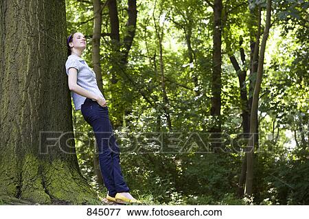 Stock Photo - A young woman leaning against a tree. Fotosearch