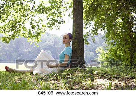 A young woman leaning against a tree next to a lake View Large Photo Image Stock Photograph - A young woman leaning against a tree next to a lake. Fotosearch