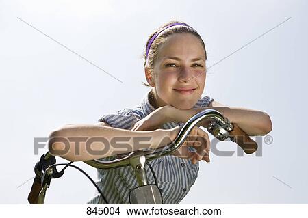 A young woman leaning on bicycle handlebars View Large Photo Image Picture - A young woman leaning on bicycle handlebars . Fotosearch