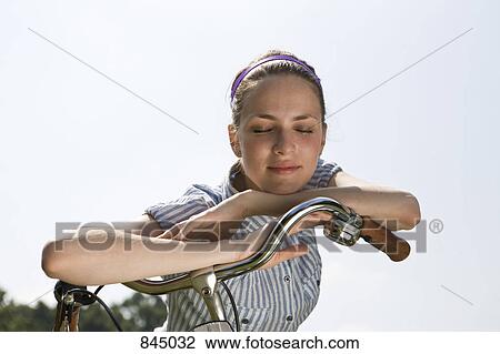 A young woman leaning on bicycle handlebars View Large Photo Image Stock Image - A young woman leaning on bicycle handlebars . Fotosearch