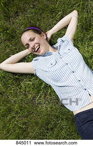 Stock Image - A young woman lying in grass laughing. Fotosearch
