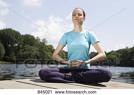 Stock Image - A young woman practicing yoga on a jetty. Fotosearch