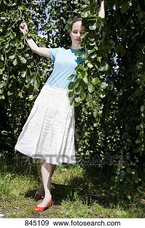 Stock Photo - A young woman standing amongst lush foliage. Fotosearch