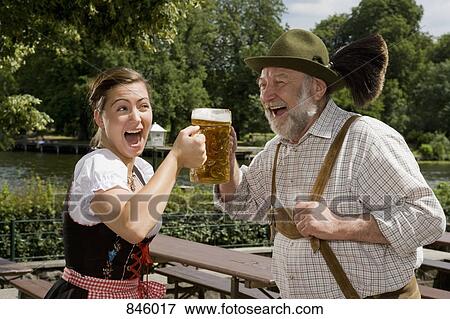 Stock Photo - A traditionally clothed German man and woman in a beer garden toasting glasses. Fotosearch
