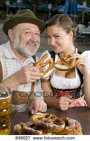 Stock Photo - A traditionally clothed German man and woman in a beer garden holding pretzels. Fotosearch
