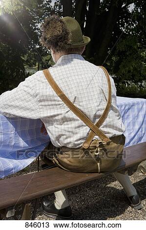Stock Image - A traditionally clothed German man in a beer garden, rear view. Fotosearch