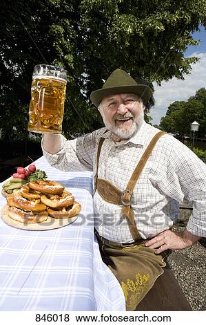 Stock Photo - A traditionally clothed German man in a beer garden raising his beer glass in toast. Fotosearch