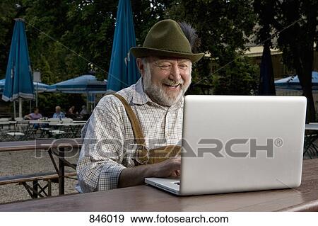 A traditionally clothed German man in a beer garden using a laptop View Large Photo Image Stock Photo - A traditionally clothed German man in a beer garden using a laptop. Fotosearch