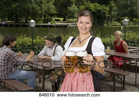A traditionally clothed German woman serving beer in a beer garden View Large Photo Image Stock Image - A traditionally clothed German woman serving beer in a beer garden. Fotosearch