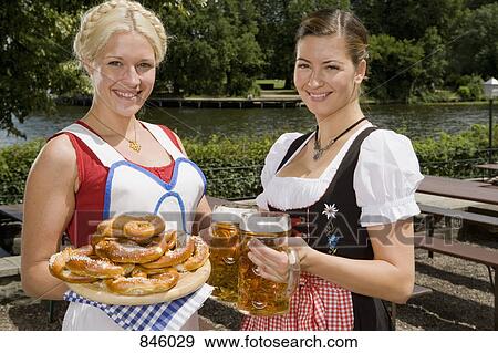 Two traditionally clothed German women serving pretzels and beer in a beer garden View Large Photo Image Stock Photo - Two traditionally clothed German women serving pretzels and beer in a beer garden. Fotosearch
