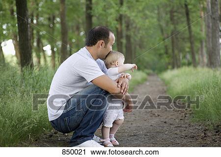 Stock Image - A father crouching with his baby daughter on a rural path. Fotosearch