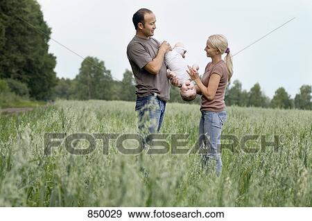 Stock Photo - Two parents playing with their daughter in a field. Fotosearch